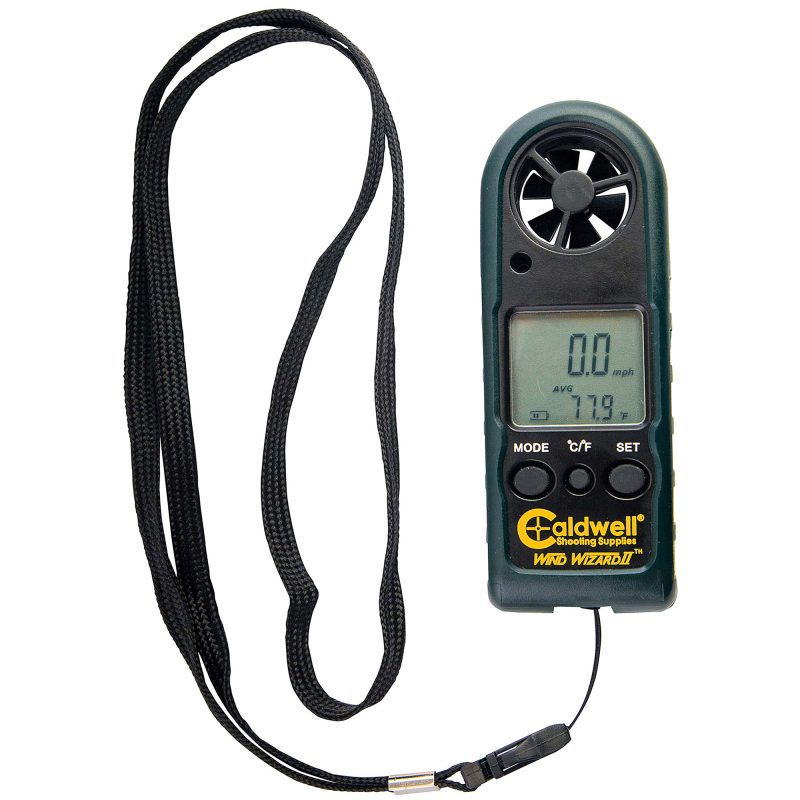 Black Caldwell Wind Wizard II handheld wind meter with LCD screen displaying readings, held in a gloved hand against an outdoor background.