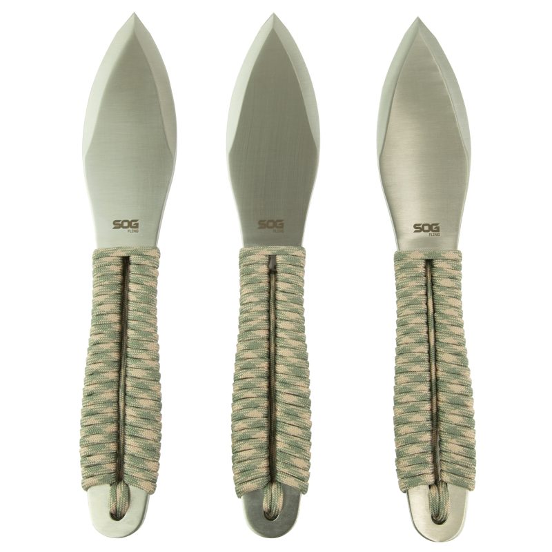 Three SOG Fling throwing knives with green and tan paracord handles, spear point blades, and a black nylon sheath, displayed on a rugged surface.