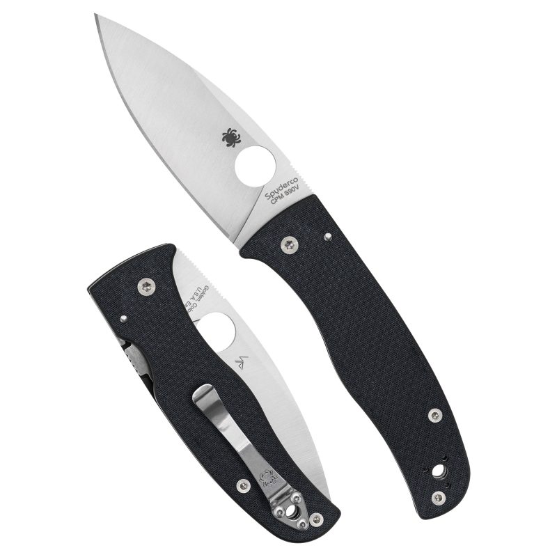 Spyderco Bodacious folding knife with a silver spear point blade and black carbon fiber handle, shown open on a rustic surface.