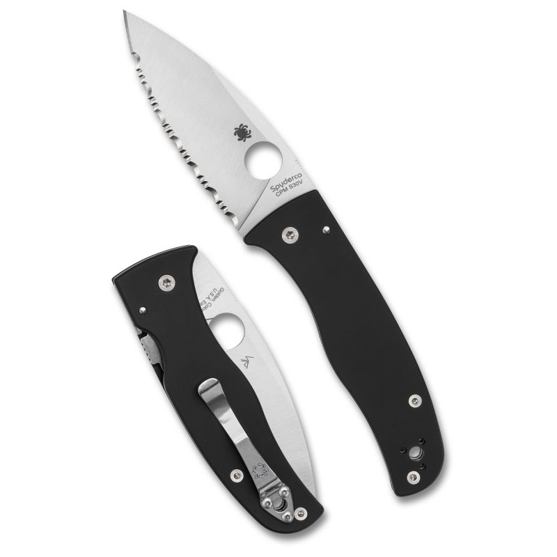 Spyderco Bodacious folding knife with black G-10 handle and satin silver serrated CPM-S30V blade, shown open on a rustic background.