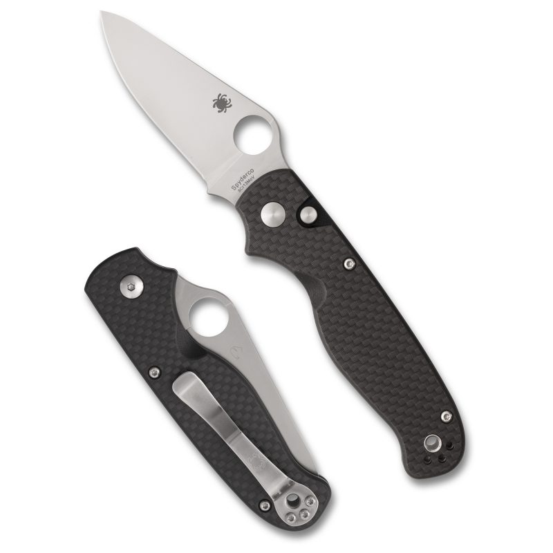 Spyderco Buttonup folding knife with a black carbon fiber handle and a silver plain edge blade, shown open on a rustic surface.
