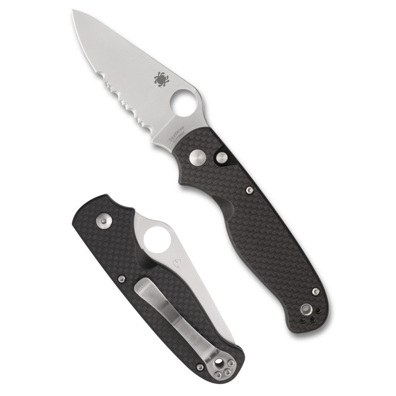 Spyderco Buttonup folding knife with a silver clip point blade and black carbon fiber handle, shown open on a rustic background.